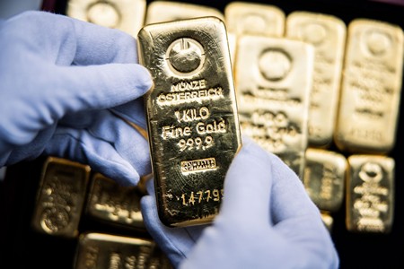 Kesztyűs kéz 1 kilós befektetési aranyrudat tart.